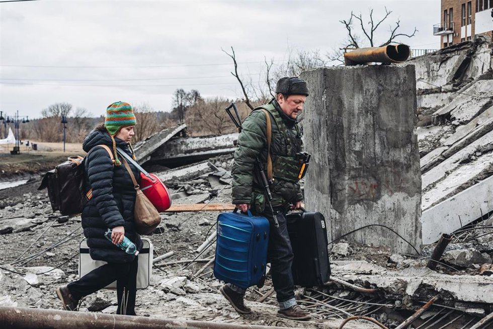 Archivo - Un voluntario armado y una mujer caminan por el puente destruido de Irpin, a 5 de marzo de 2022.