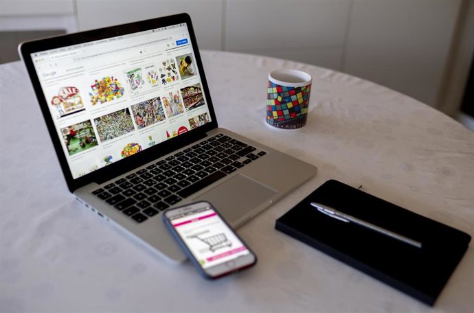 Archivo - Una persona compra con su teléfono móvil y ordenador