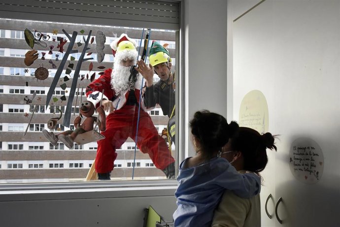 Papá Noel saluda a un niña ingresada para darle un regalo mientras se descuelga por la fachada del Hospital Universitario Germans Trias i Pujol (Can Ruti), a 19 de diciembre de 2022, en Badalona, Barcelona, Catalunya (España). Durante estas fechas navid