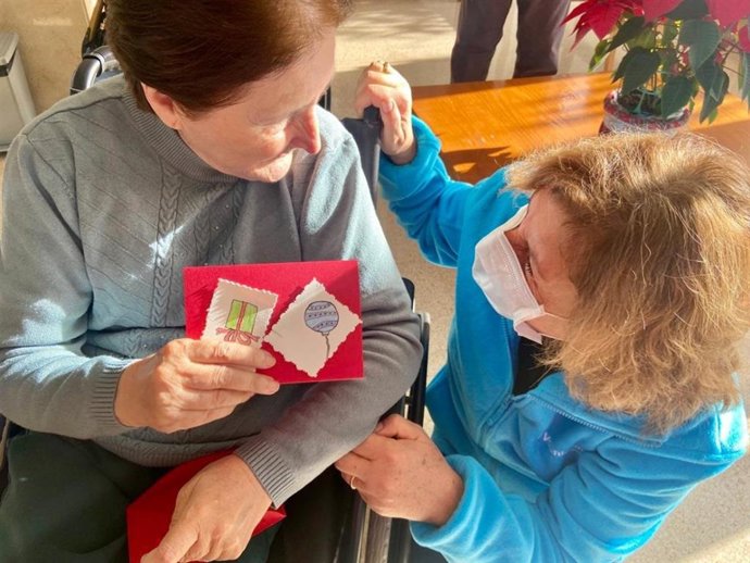 Una persona mayor sostiene una de las postales navideñas elaborada por voluntarios.