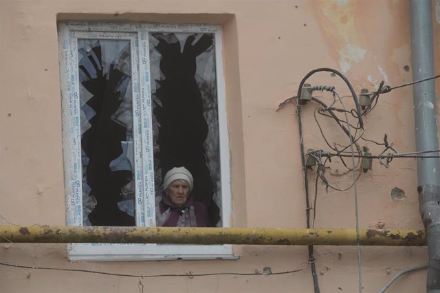 Archivo - Una mujer mayor es vista a través de una ventana rota de un edificio residencial, dañado como resultado de un bombardeo, en Donetsk, República Popular de Donetsk. 