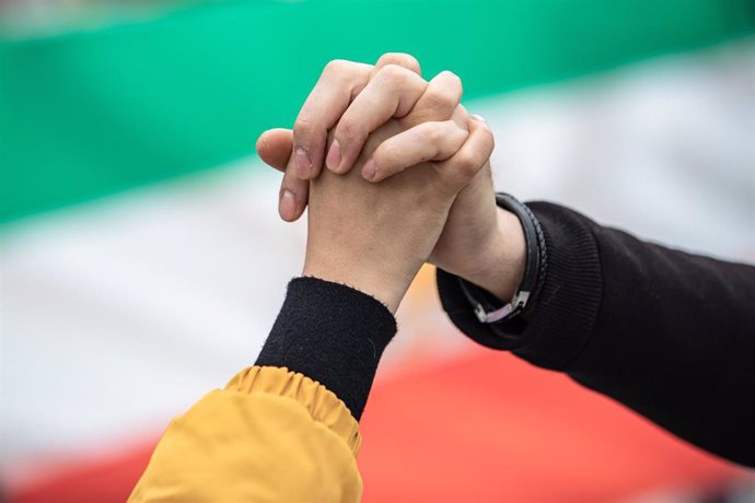 Dos manos unidas frente a una bandera de Irán 