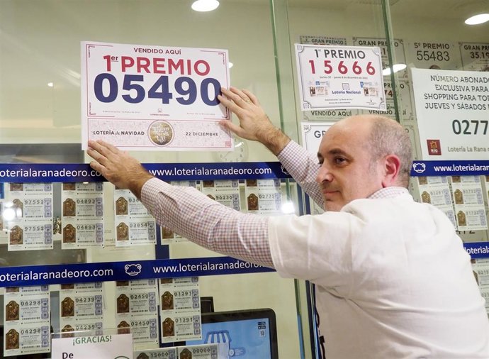 El propietario de la administración de Lotería de Parquesol coloca el cartel con el número del 'Gordo' de 2022.