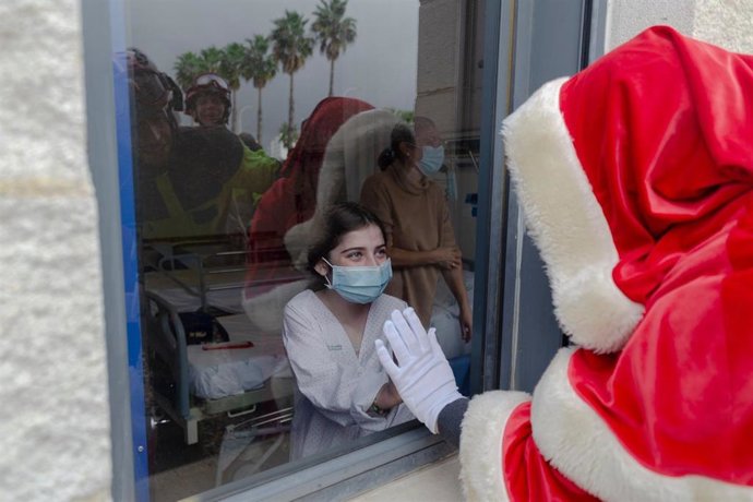 Papá Noel saluda por una ventana a una niña ingresada en el Hospital Juan Ramón Jiménez de Huelva desde el camión escala de los bomberos.