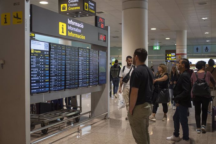 Archivo - Varias personas observan un panel de llegadas en el aeropuerto de Barcelona, en Catalunya (España). 