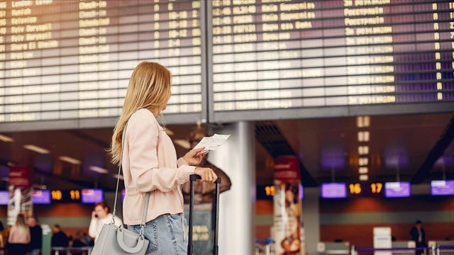 Viajera mirando billete frente a panel de información en un aeropuerto