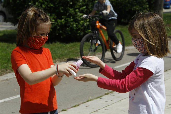 Archivo - Dos niñas con mascarillas se limpian las manos con solución hidroalcohólica.
