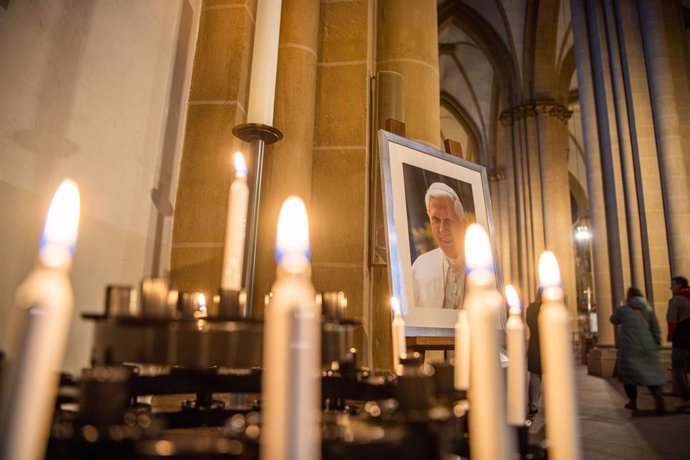28 December 2022, North Rhine-Westphalia, Paderborn: A portrait of Pope Emeritus Benedict XVI stands behind devotional candles in Paderborn Cathedral. Photo: Lino Mirgeler/dpa - ATTENTION: only for use in full format