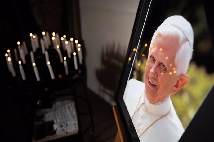 31 December 2022, North Rhine-Westphalia, Paderborn: Candles can be seen in front of a picture with Pope Emeritus Benedict XVI stands in the Cathedral of St. Mary, St. Liborius, St. Kilian of Paderborn. Pope Emeritus Benedict XVI, who was the first pope