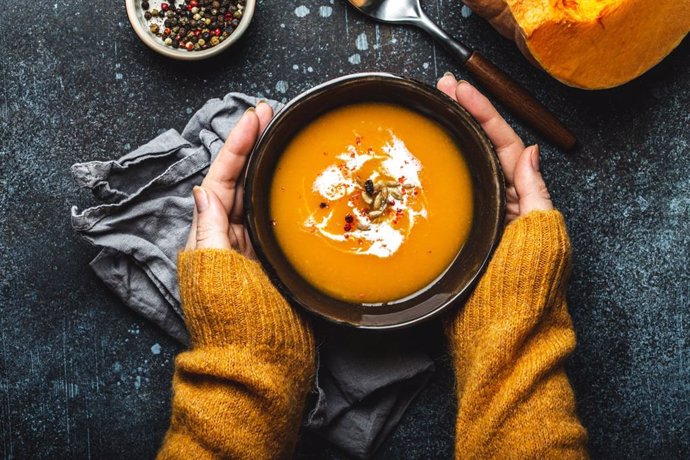 Archivo - Mujer calentándose las manos con un plato de crema de calabaza.