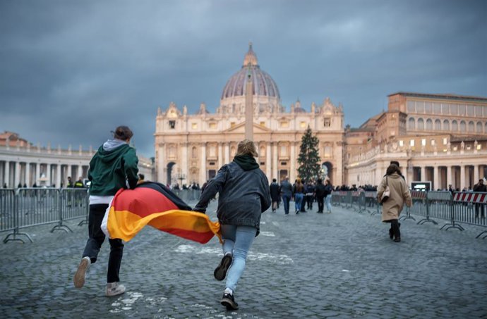 02 January 2023, Vatican, Vatican City: Two young people with a Germany flag sprint across St. Peter's Square in front of St. Peter's Basilica after the death of Pope Emeritus Benedict XVI. Photo: Michael Kappeler/dpa