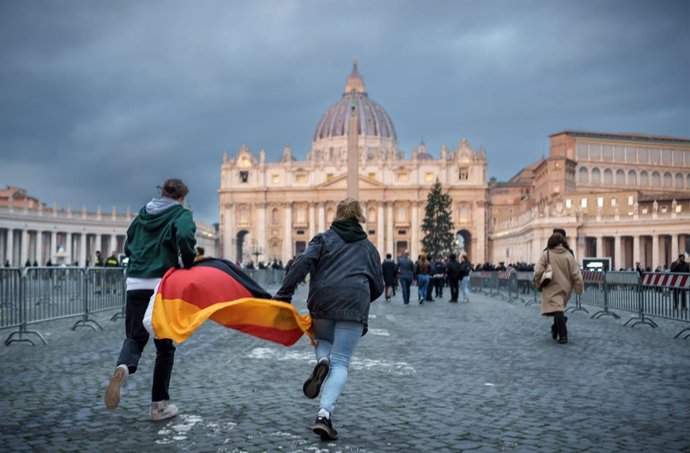02 January 2023, Vatican, Vatican City: Two young people with a Germany flag sprint across St. Peter's Square in front of St. Peter's Basilica after the death of Pope Emeritus Benedict XVI. Photo: Michael Kappeler/dpa