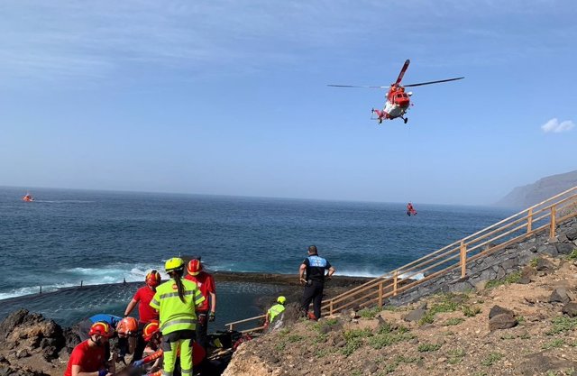 Efectivos del Consorcio de Bomberos de Tenerife y personal del Servicio de Urgencias Canario asiste a uno de los afectados mientras el helicóptero del GES procede al rescate de la joven