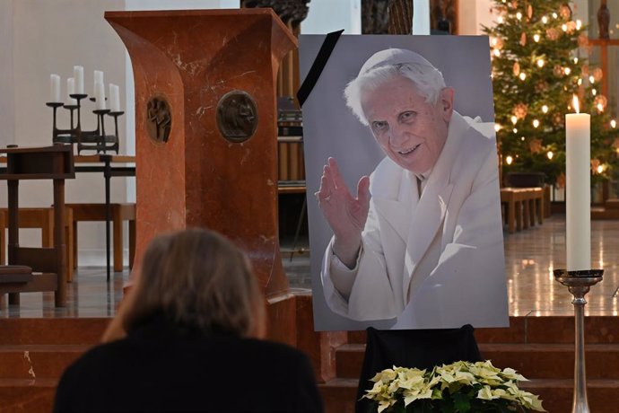 31 December 2022, Bavaria, Munich: A woman prays in front of a picture of the late Pope Emeritus Benedict XVI at the Frauenkirche church in Munich. Pope Emeritus Benedict XVI died 31 December 2022, at the Vatican at the age of 95. Photo: Katrin Requadt/