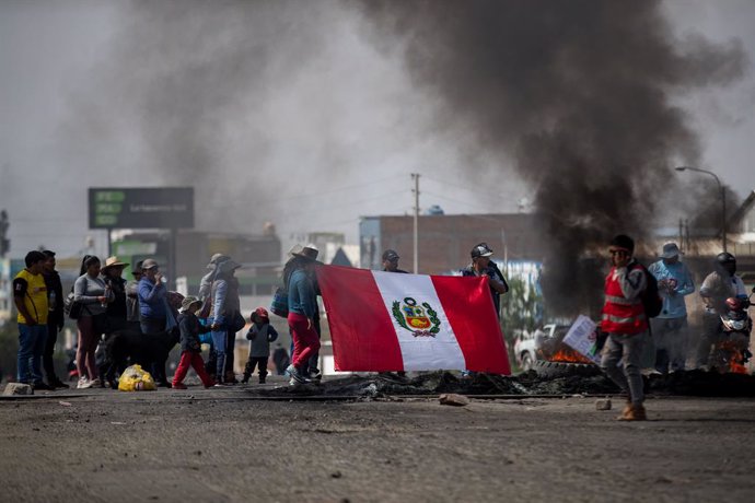 14 December 2022, Peru, Arequipa: Demonstrators hold up a Peruvian flag next to burning tires during a protest. The Peruvian government has declared a state of emergency across the country in the face of increasingly violent protests against the ouster 