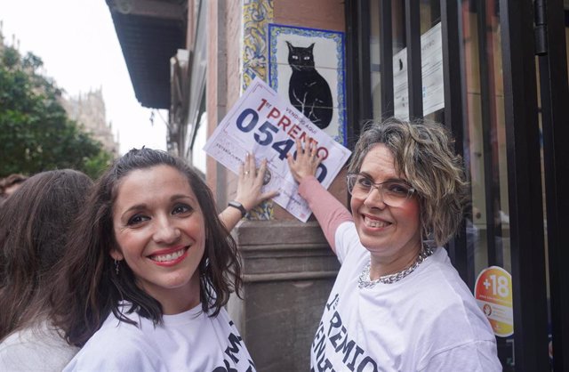 Dos empleadas de la administración de Loterías de 'El Gato Negro', con el número del primer premio del sorteo extraordinario de Navidad.