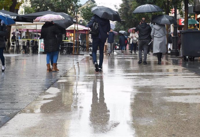 Personas caminan por la calle con paraguas.