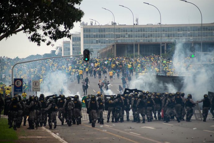08 January 2023, Brazil, Brasilia: Supporters of former Brazilian President Jair Bolsonaro clash with law enforcement officers in the capital, who form a chain behind barriers and fire tear gas grenades at the demonstrators. Supporters of former Brazili