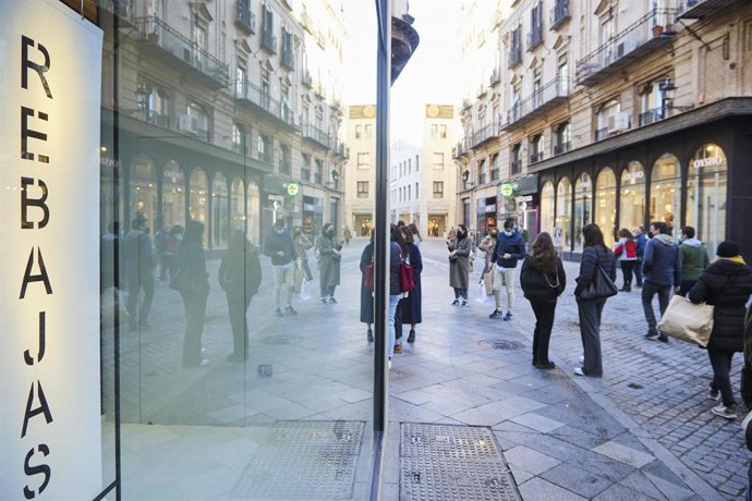 Archivo - Detalle de un cartel de rebajas y varias personas esperando que abran los negocios durante el primer día de las rebajas, Sevilla, foto de archivo