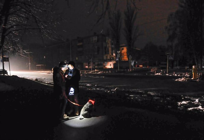 Archivo - Dos personas se alumbran con un teléfono móvil en una calle oscura de Kiev