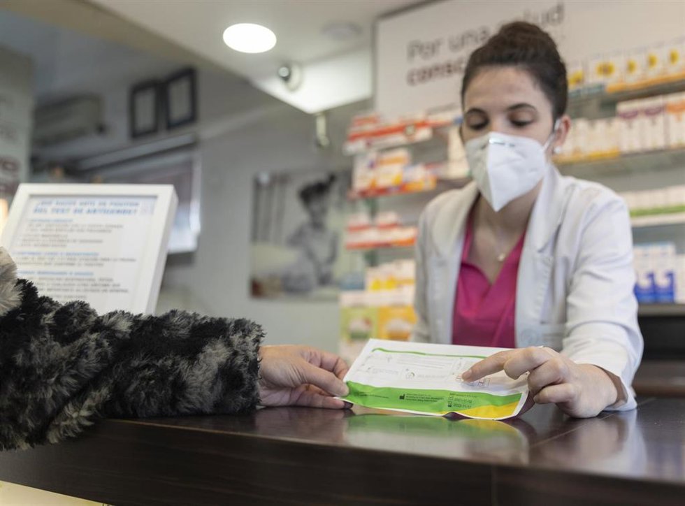 Archivo - Una farmacéutica muestra un test de antígenos a una persona en la farmacia Las Gemelas.