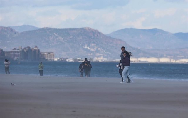 Varias personas caminan por la playa mientras les da el viento