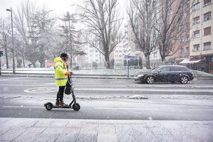 Un hombre con un monopatín circula por una calle de Vitoria-Gasteiz cubierta de nieve