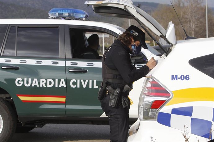 Archivo - Un agente de Policía Local, junto a un vehículo del cuerpo, y detrás, un vehículo de la Guardia Civil.