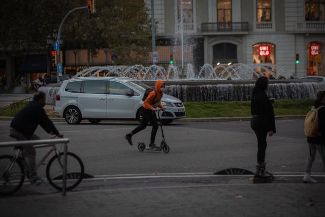 Archivo - Un hombre en bici y un joven en patinete en Barcelona. Archivo.