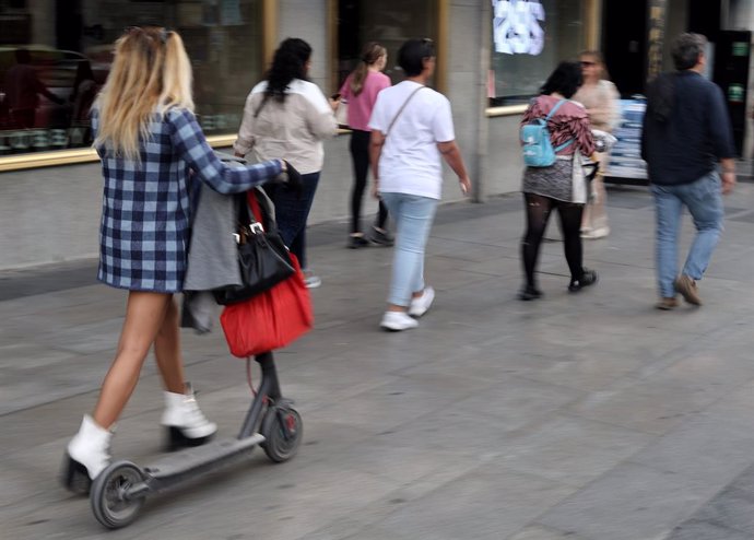 Archivo - Una mujer camina con un patinete eléctrico, a 3 de octubre de 2022, en Madrid (España). 