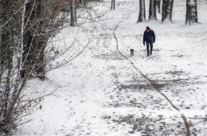 Un hombre pasea a su perro en un parque cubierto de nieve en Burgos.