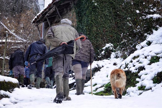 Varias personas caminan por una calle nevada, a 18 de enero de 2023, en San Juan de Beleño, Ponga, Asturias (España). La Agencia Estatal de Meteorología (Aemet) ha elevado a naranja el nivel de alarma en Asturias, tanto por fenómenos costeros, como por ac