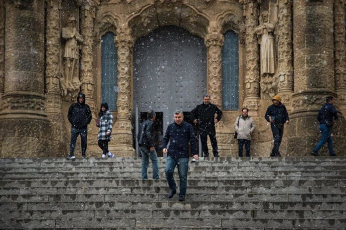 Varias personas en el Tibidabo de Barcelona mientras caen copos de nieve.