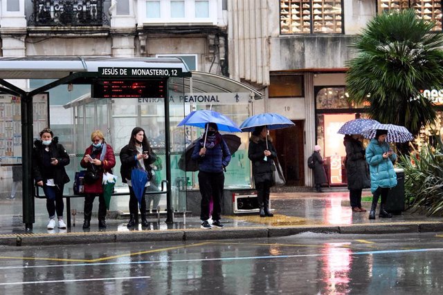 Varias personas con paraguas en una parada de autobús de Santander