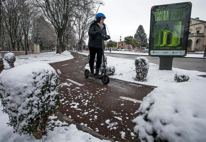 Una mujer conduce un patinete eléctrico por una calle cubierta de nieve, a 18 de enero de 2023, en Burgos, Castilla y León (España). La provincia está en alerta debido a que la cota de nieve ha bajado a los 400 metros y se esperan nevadas generalizadas.