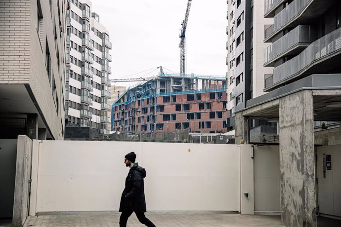 Archivo - Un hombre pasa por delante de una obra, en construcción, parada por falta de suministros como el hormigón, en Vallecas