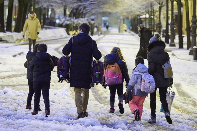 Varios niños van al colegio caminando por la nieve.