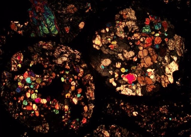 Sección fina de un meteorito al microscopio. Los distintos colores representan diferentes minerales, porque la luz viaja a través de ellos de diferentes maneras.