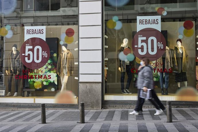 Archivo - Una persona pasa delante de un escaparate de un comercio con carteles de rebajas.