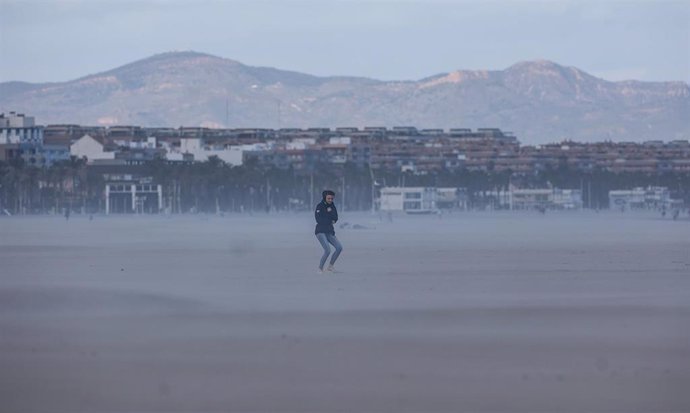 Una mujer camina por la playa mientras le da el viento