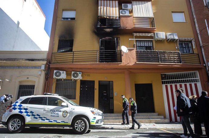 Dos policías entran en el edificio en el que han fallecido tres personas y varias más han resultado heridas en el incendio de una vivienda en Huelva.