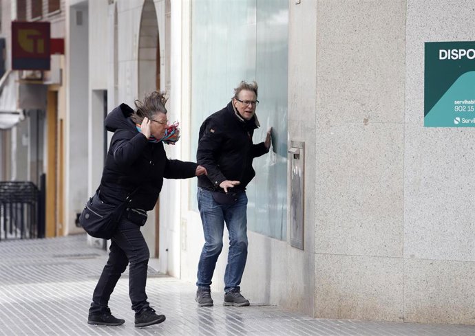 Varias personas intentan andar por la calle donde el temporal con vientos de 70 km/h y el litoral malagueño registra olas de tres metros