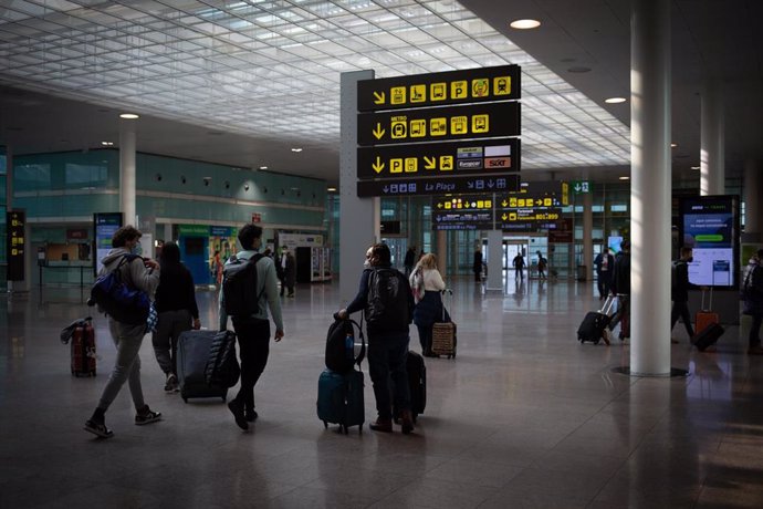 Archivo - Varias personas caminan con su equipaje en el interior del Aeropuerto de Barcelona-El Prat.