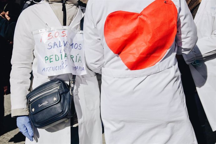 Dos personas protestan con un cartel que reza '¡S.O.S.! Salvemos la pediatría de Atención Primaria'