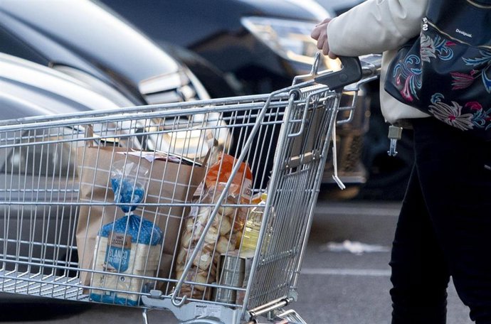 Archivo - Una mujer sale de un supermercado con un carro de la compra