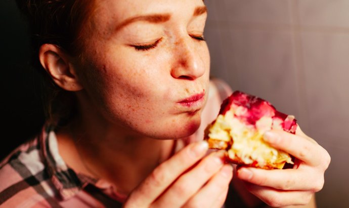 Archivo - Portrait of a red-haired woman in her kitchen. She afforded herself a slice of raspberry pie. She eats the cake with her hands. She enjoys this moment.