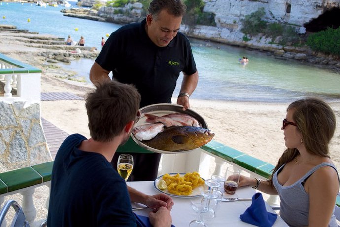 Archivo - Un camarero presenta pescado fresco a los comensales en un restaurante en Cala Alcaufar (Sant Lluís, Menorca)