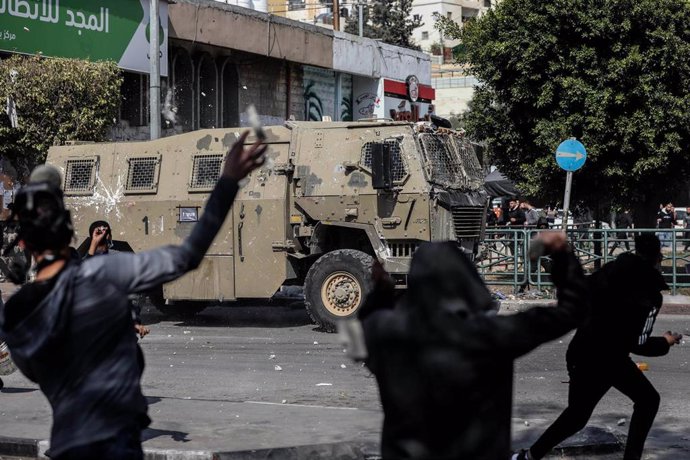 Un grupo de palestinos lanzan piedras contra un vehículo militar de Israel durante los enfrentamientos en la ciudad cisjordana de Nablús por una redada del Ejército israelí