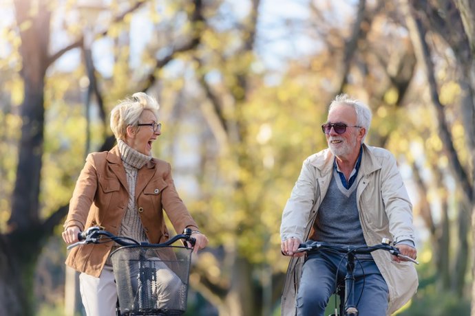 Archivo - Alegre pareja de personas mayores en bicicleta en el parque.
