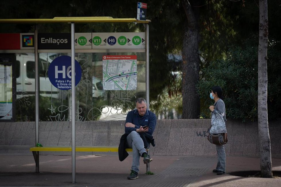 Archivo - Dos personas esperan el autobús en Barcelona, en una foto de archivo.
